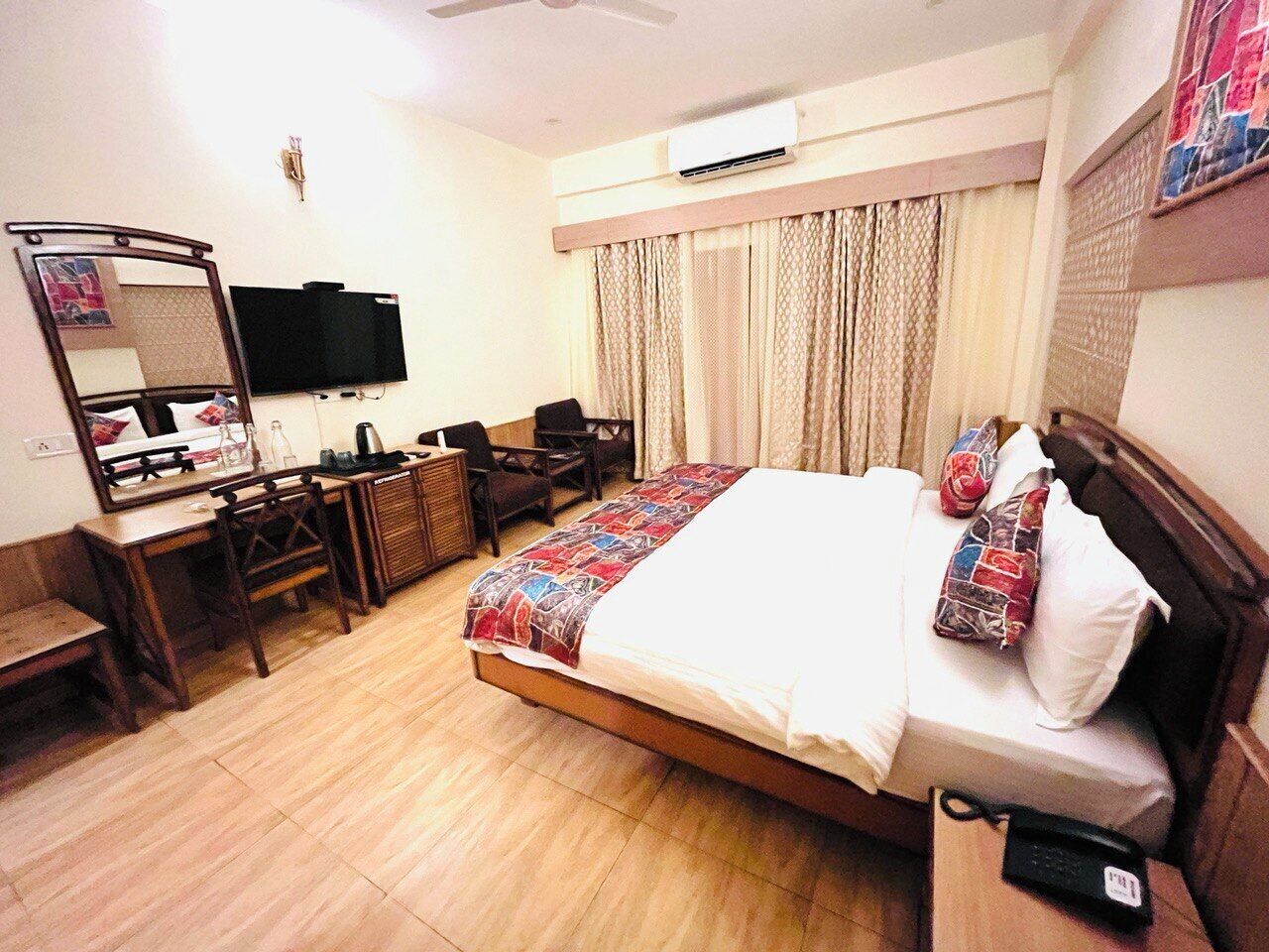 Quarto de hotel com cama, escrivaninha com cadeira, espelho, televisão e ar condicionado.