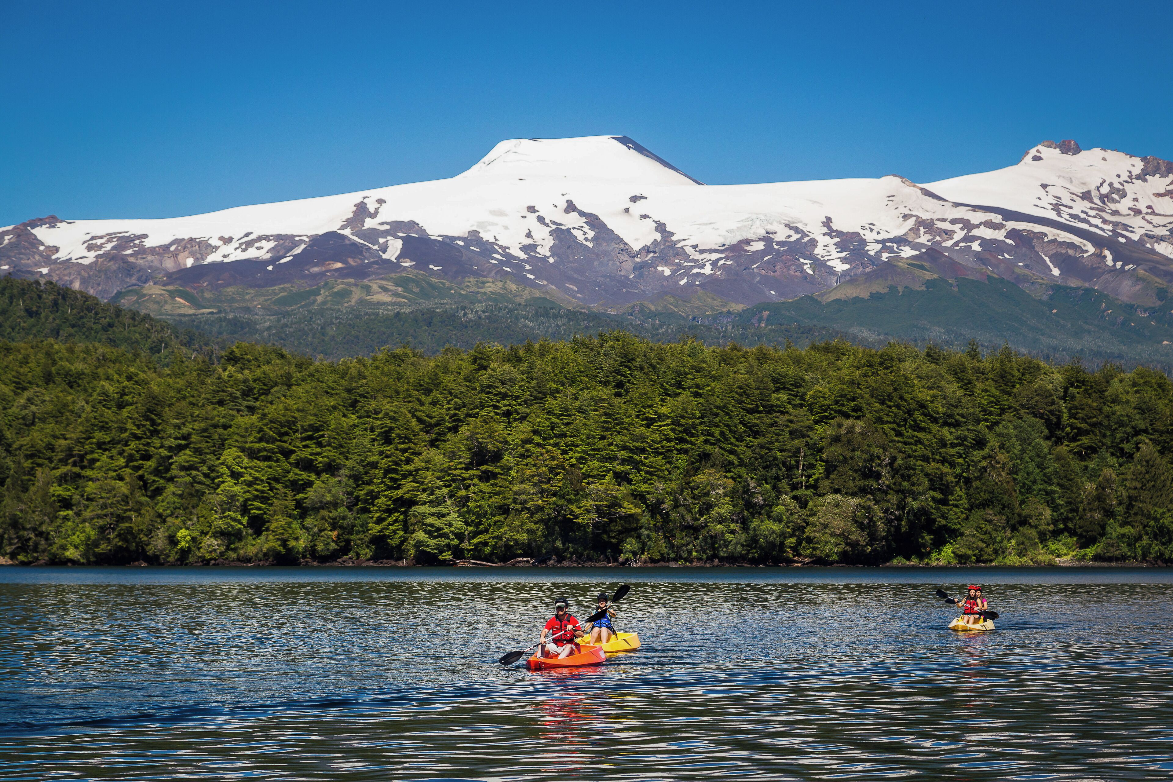 Kayakers on a calm lake with a snow-capped mountain in the background.