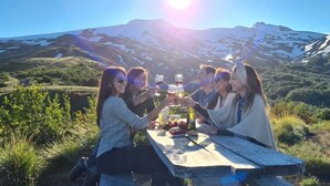 A group of people sitting at a wooden table outdoors with a mountain in the background. - Neltume Lodge (Panguipulli)