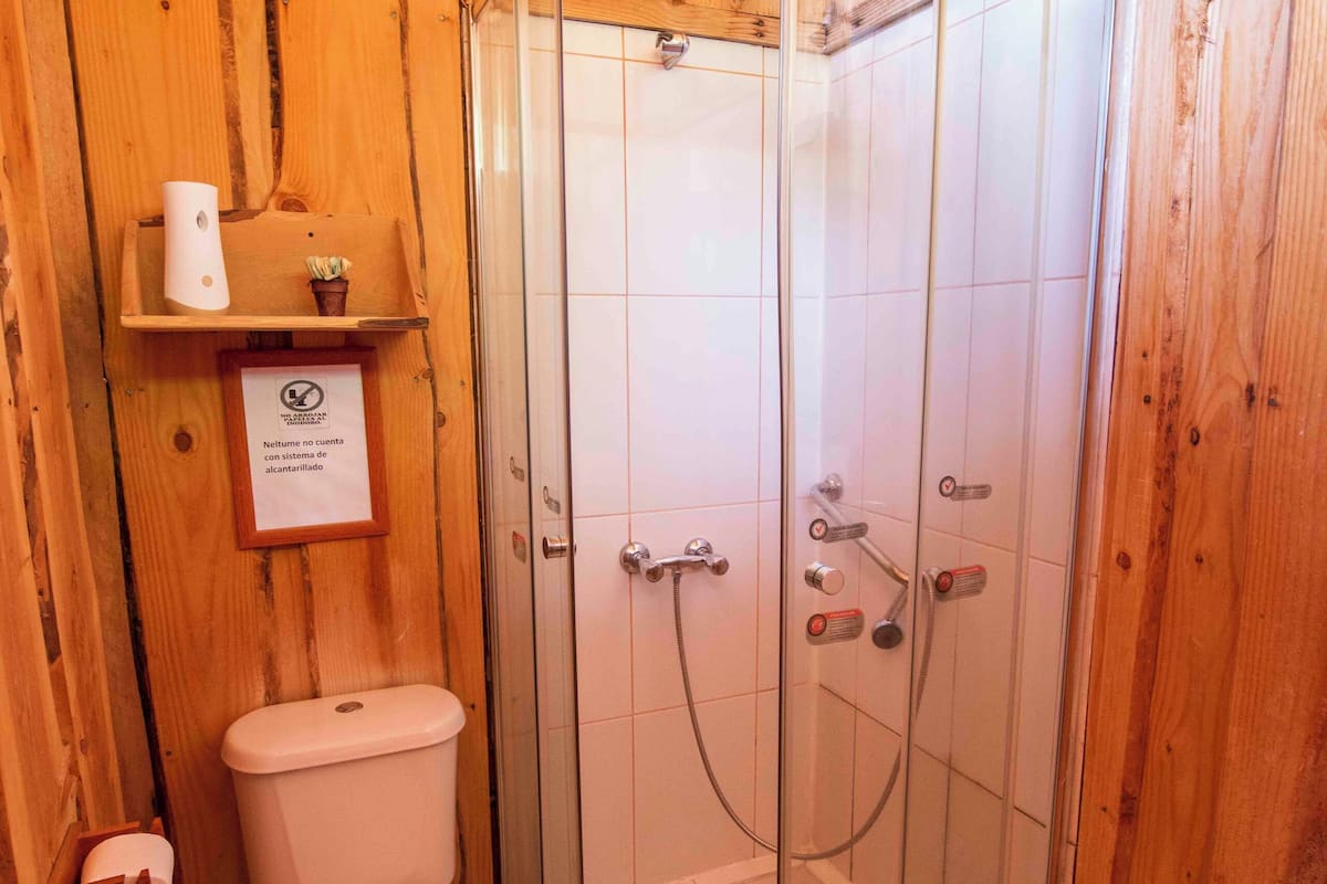 A wooden-paneled bathroom with a glass-enclosed shower, a toilet, and a shelf with toiletries.