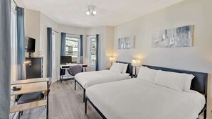 Une chambre d’hôtel avec deux lits, un bureau, une chaise, une télévision et des œuvres d’art accrochées aux murs.