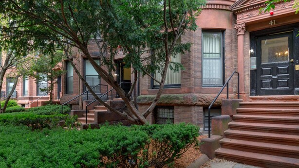A brick building with a black front door, a staircase, and a well-maintained garden.