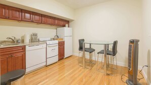 A compact kitchen with wooden cabinets, a refrigerator, a stove, and a dining area with a glass table and chairs.