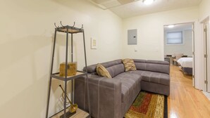 A modern living room with a gray sectional sofa, a wooden floor, and a small shelf with decorative items.
