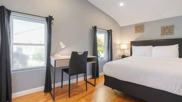 A modern hotel room with a large bed, a desk with a chair, and a window with curtains.