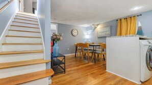 A staircase leading to a dining area with a table and chairs, a clock on the wall, and a washing machine in the corner. - Well Located 3 Bed, 1 Bath in Kendall Sq (Cambridge)