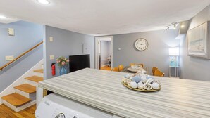 A modern kitchen with a striped countertop, wooden staircase, and a dining area with a table set for a meal. - Well Located 3 Bed, 1 Bath in Kendall Sq (Cambridge)