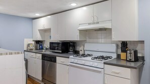 A compact kitchen with white cabinets, a gas stove, a microwave, and a dishwasher. - Well Located 3 Bed, 1 Bath in Kendall Sq (Cambridge)