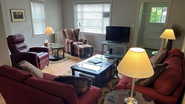 A living room with a red sofa, a striped armchair, a glass coffee table, and a television. - Spacious 2BR Apt in the Heart of Fargo (Fargo)