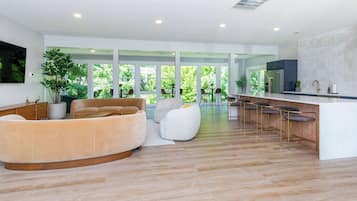 A modern kitchen with a bar area, large windows, and a seating area with sofas and chairs.