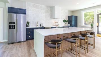 A modern kitchen with a large island, bar stools, a refrigerator, and a window with a view.