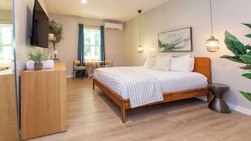 A modern bedroom with a wooden bed, a flat-screen TV, a desk, and a dining area.