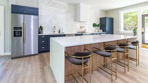 A modern kitchen with a large island, bar stools, a refrigerator, and a window with a view.