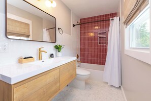 Un baño con lavamanos blanco, tocador de madera, inodoro, bañera y cortina de ducha.