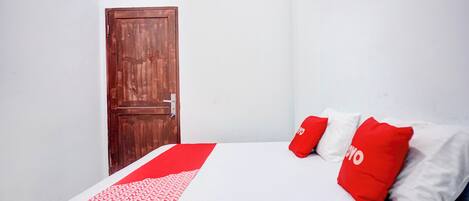 A room with a wooden door, a bed with white and red bedding, and a patterned red and white blanket.