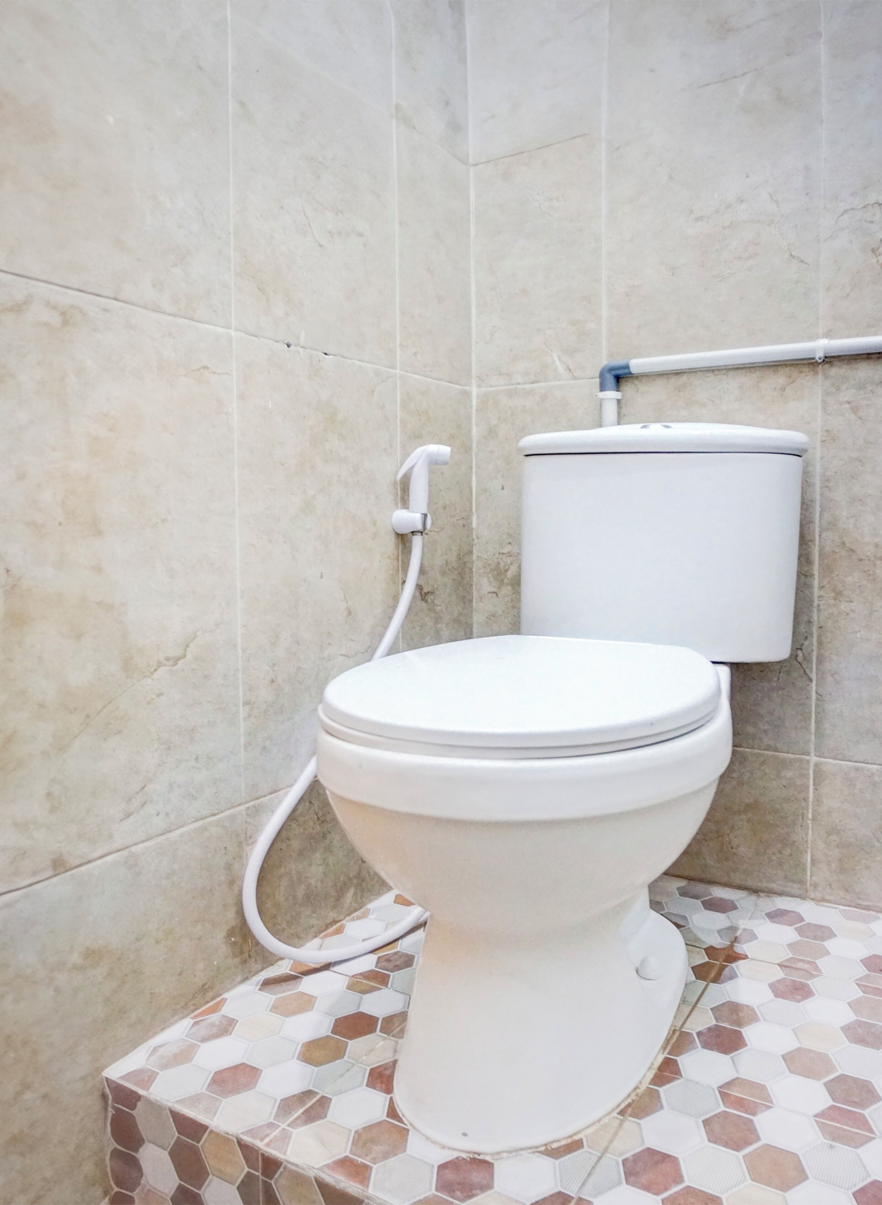 A toilet with a white tank and lid, a white flush handle, and a white pipe.