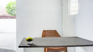 A small, modern room with a single wooden chair and a table, a potted plant on the table, and a window with blinds.