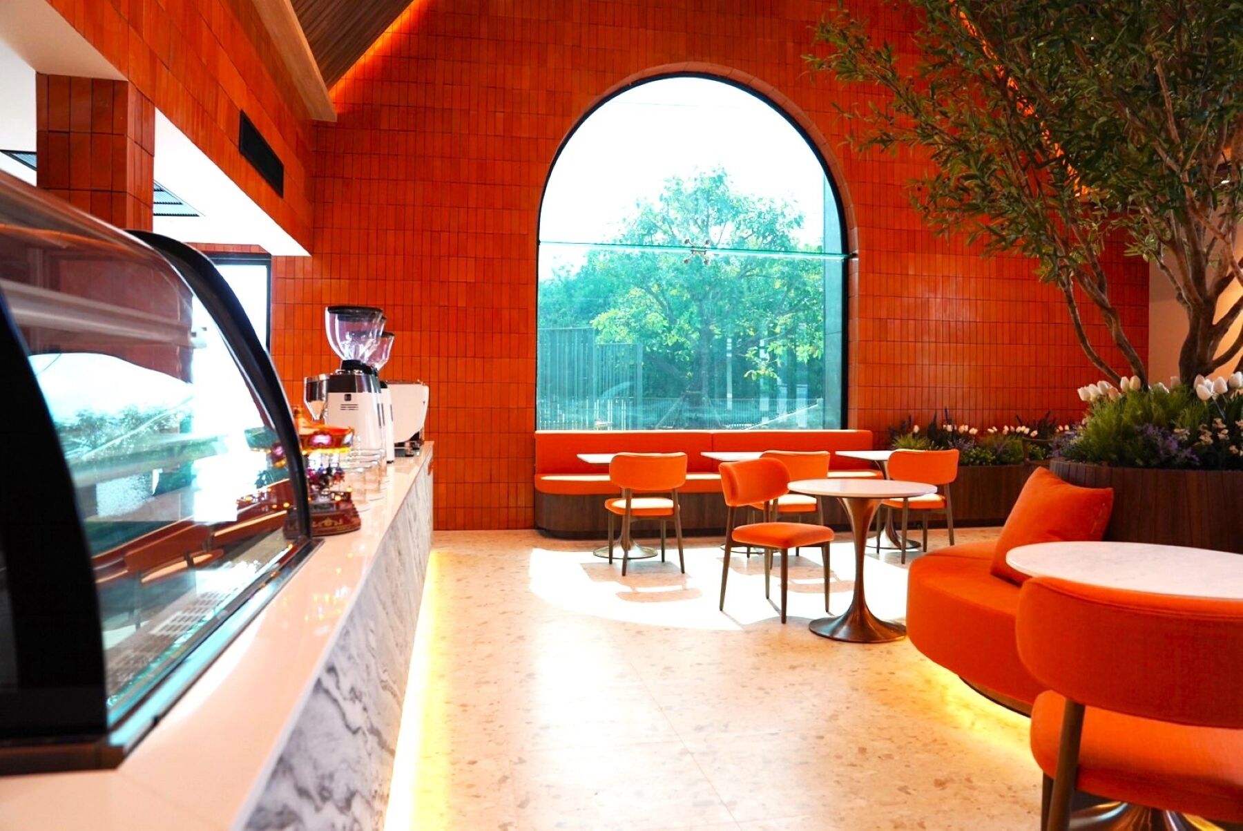 Un interior moderno con un amplio ventanal de arco, asientos color naranja y una cafetera.