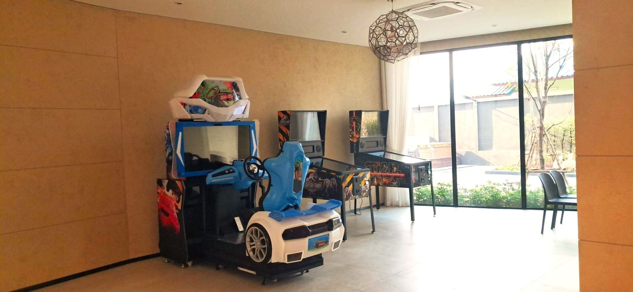 A room with a gaming chair, a table with a game, and a large window with a view of the outside.