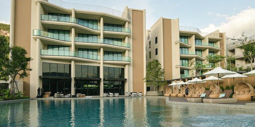 Un hotel moderno con piscina, zona de estar exterior y varios balcones.