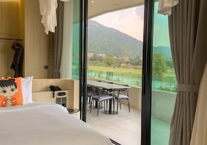 A hotel room with a bed, a table with chairs, a telephone, and a view of a mountainous landscape through large windows. - Viewpoint Khaoyai Hotel (Pak Chong)