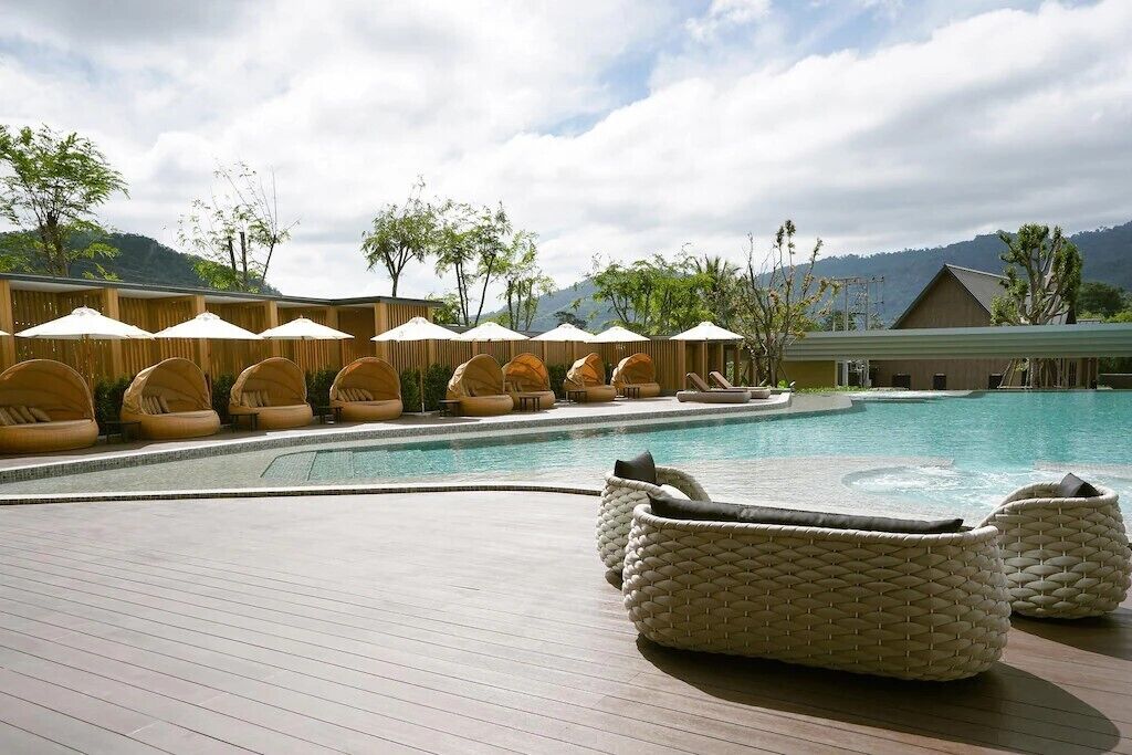 A poolside area with lounge chairs and umbrellas, surrounded by a wooden deck and a mountain backdrop.