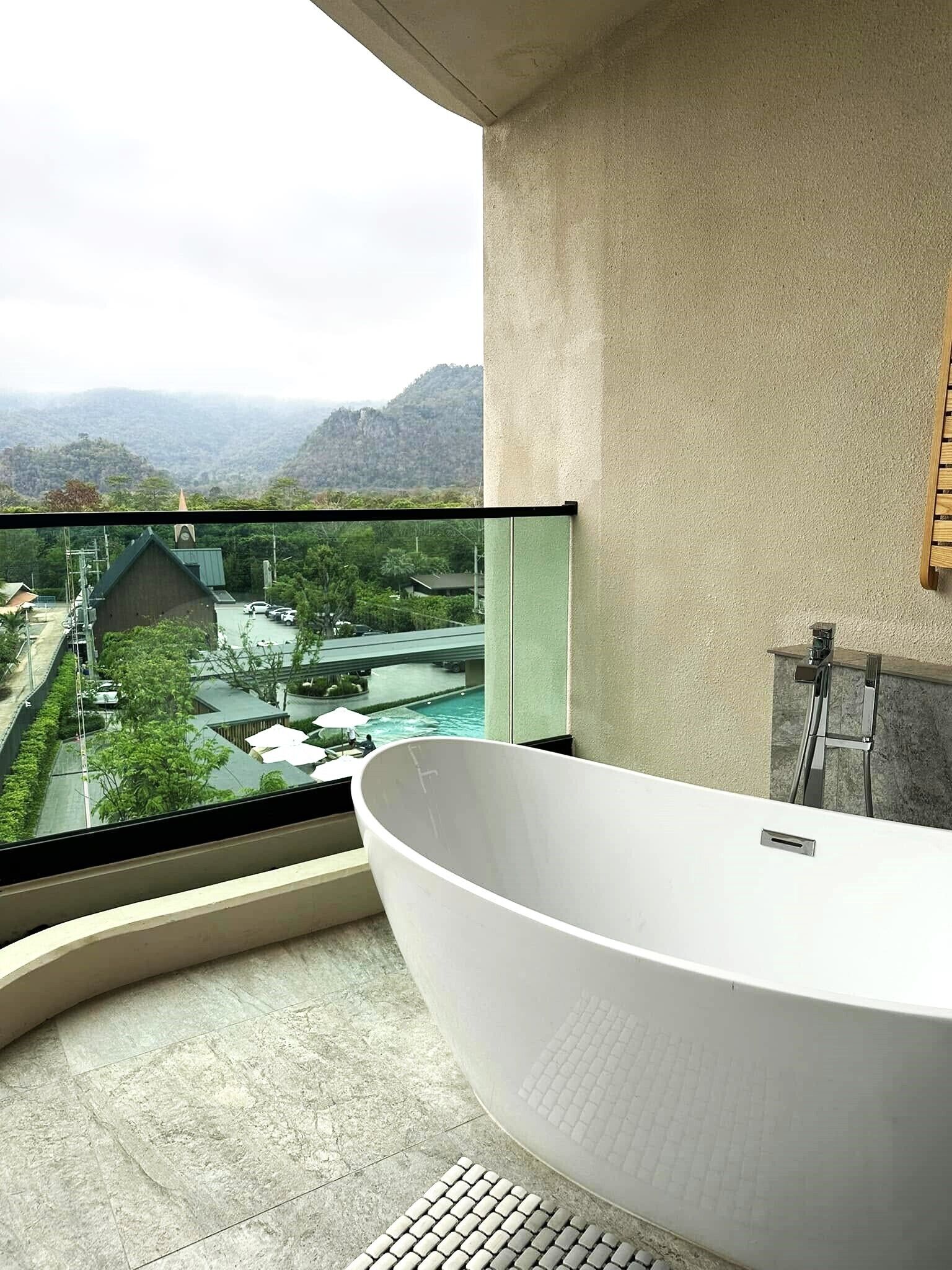 Un baño moderno con una bañera independiente, un balcón de cristal y vistas a un paisaje montañoso.