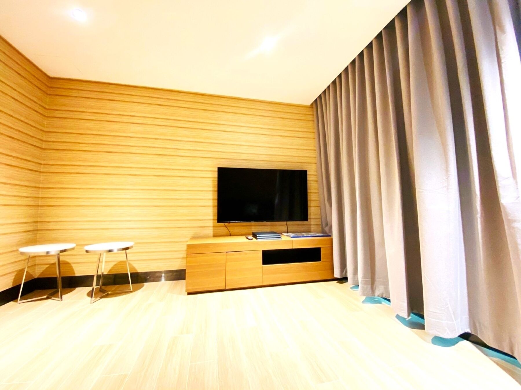 Uma sala de estar moderna com parede de madeira, uma TV de tela plana, um móvel para entretenimento de madeira e duas pequenas mesas brancas.