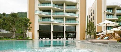 A modern hotel with a pool area, multiple balconies, and outdoor seating with umbrellas.