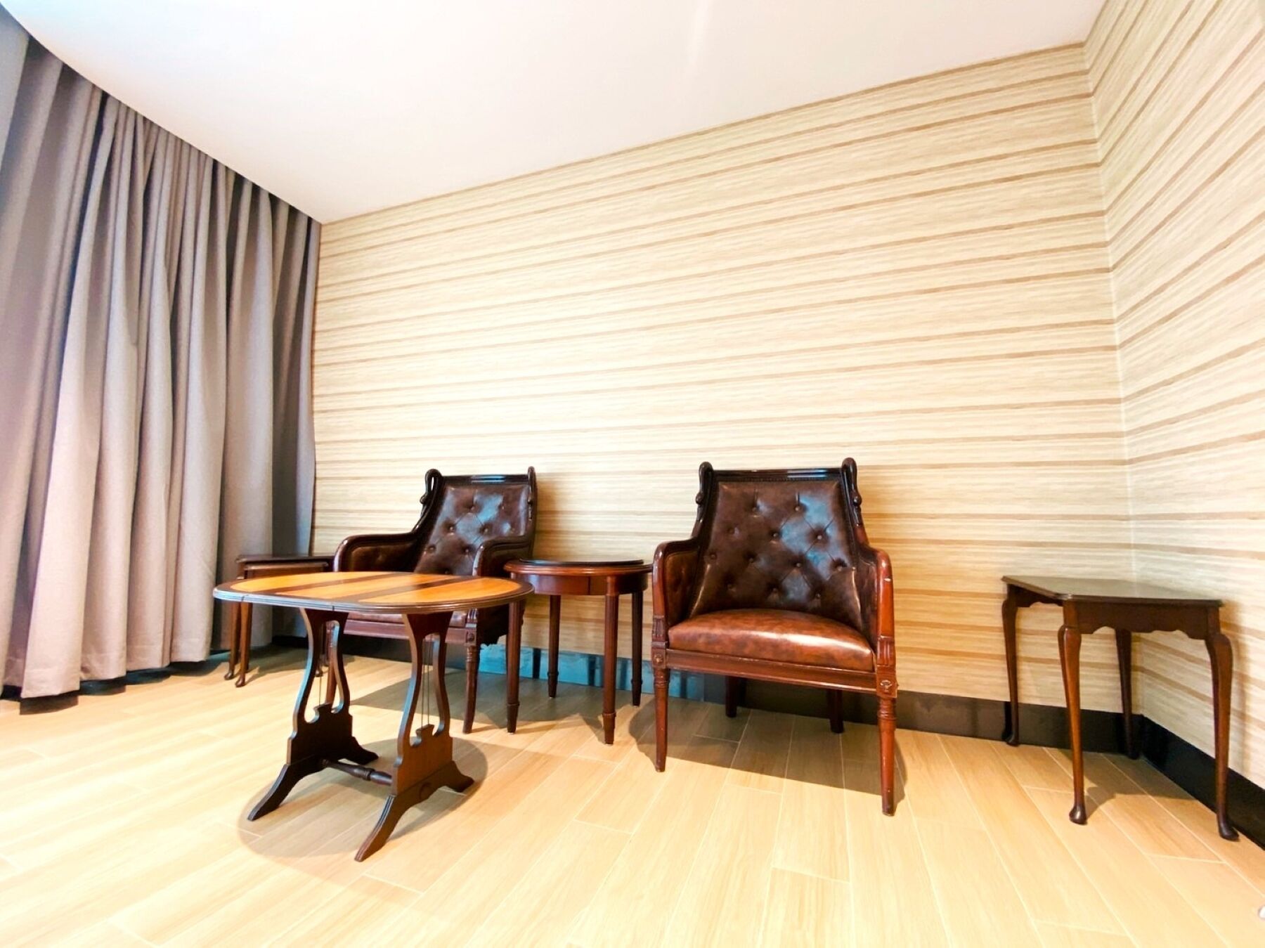 Een kamer met twee leren fauteuils, een houten salontafel en een klein bijzettafeltje. De vloer is van hout en de wand heeft een strepenpatroon.