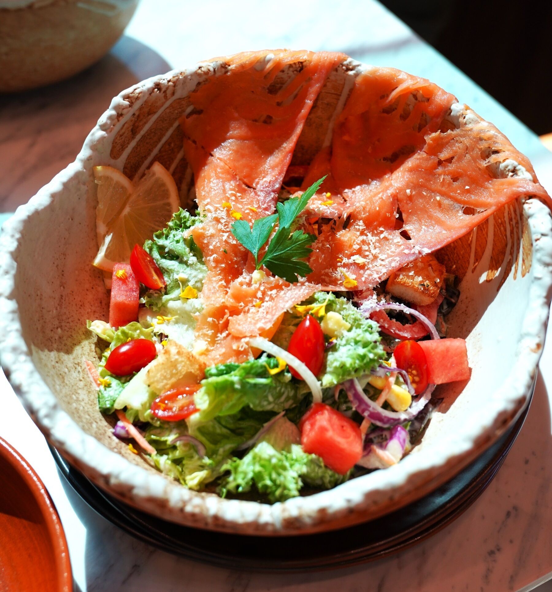 A bowl of salad with various vegetables and a piece of salmon.