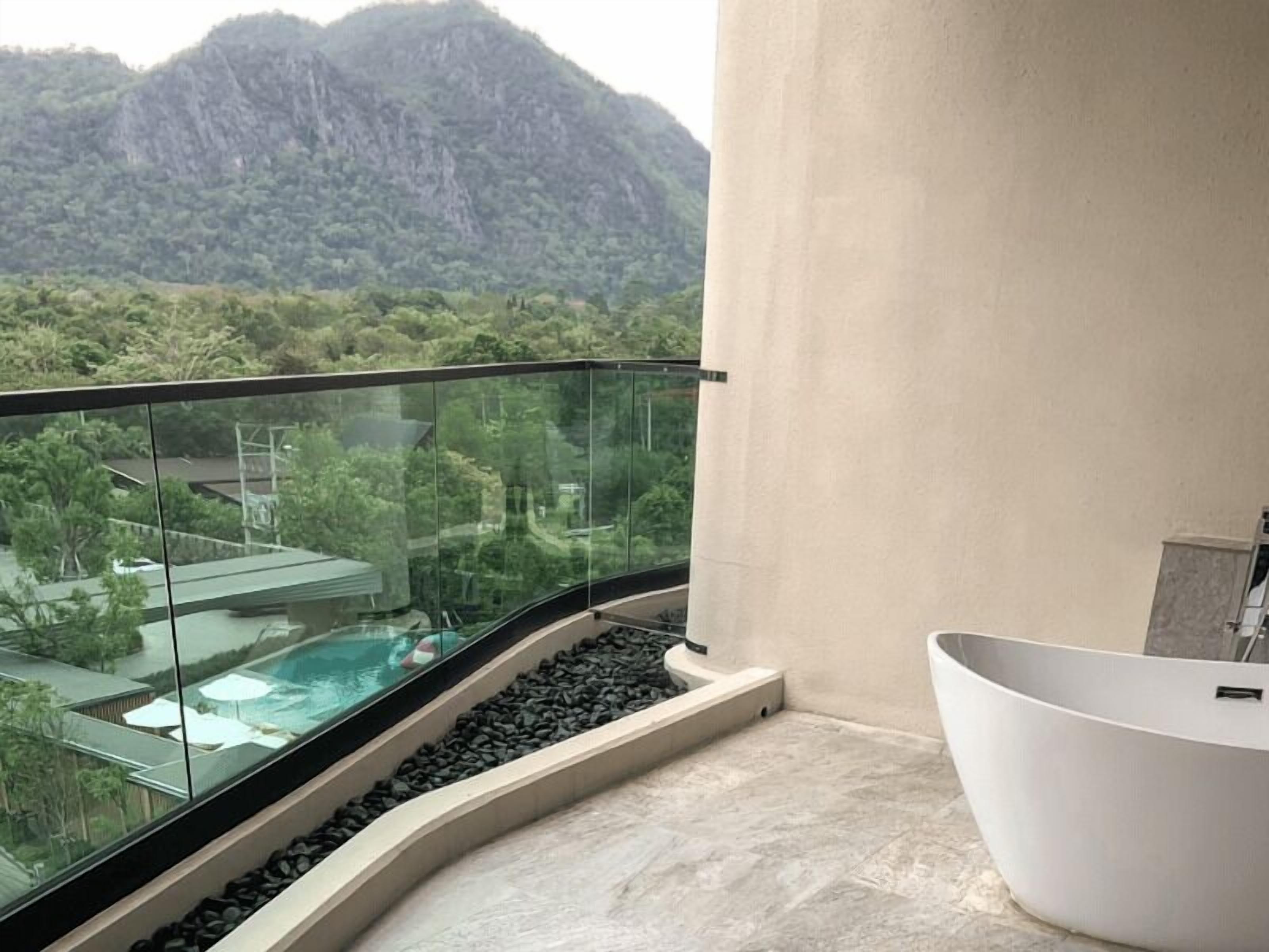 A modern bathroom with a freestanding bathtub, a glass-enclosed balcony with a view of a mountain and resort buildings.