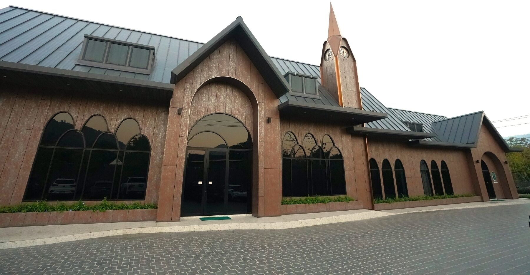 A modern building with a prominent clock tower, large arched windows, and a metal roof.