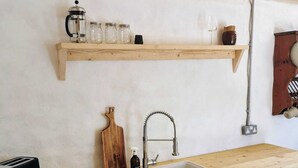 Una cocina con mostrador de madera, pileta, cocina y una alacena con frascos y una cafetera.