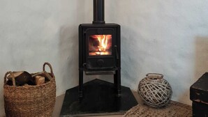 Una habitación con un horno a leña de madera oscura, una cesta tejida con leña, y otra cesta en el suelo.