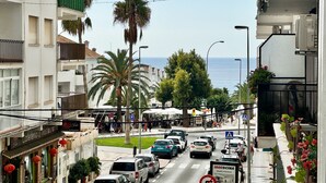 Vista de la calle con un café a la izquierda, coches en la carretera y el mar al fondo.