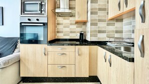 Cocina compacta con armarios de madera, microondas, horno y pileta de acero inoxidable.