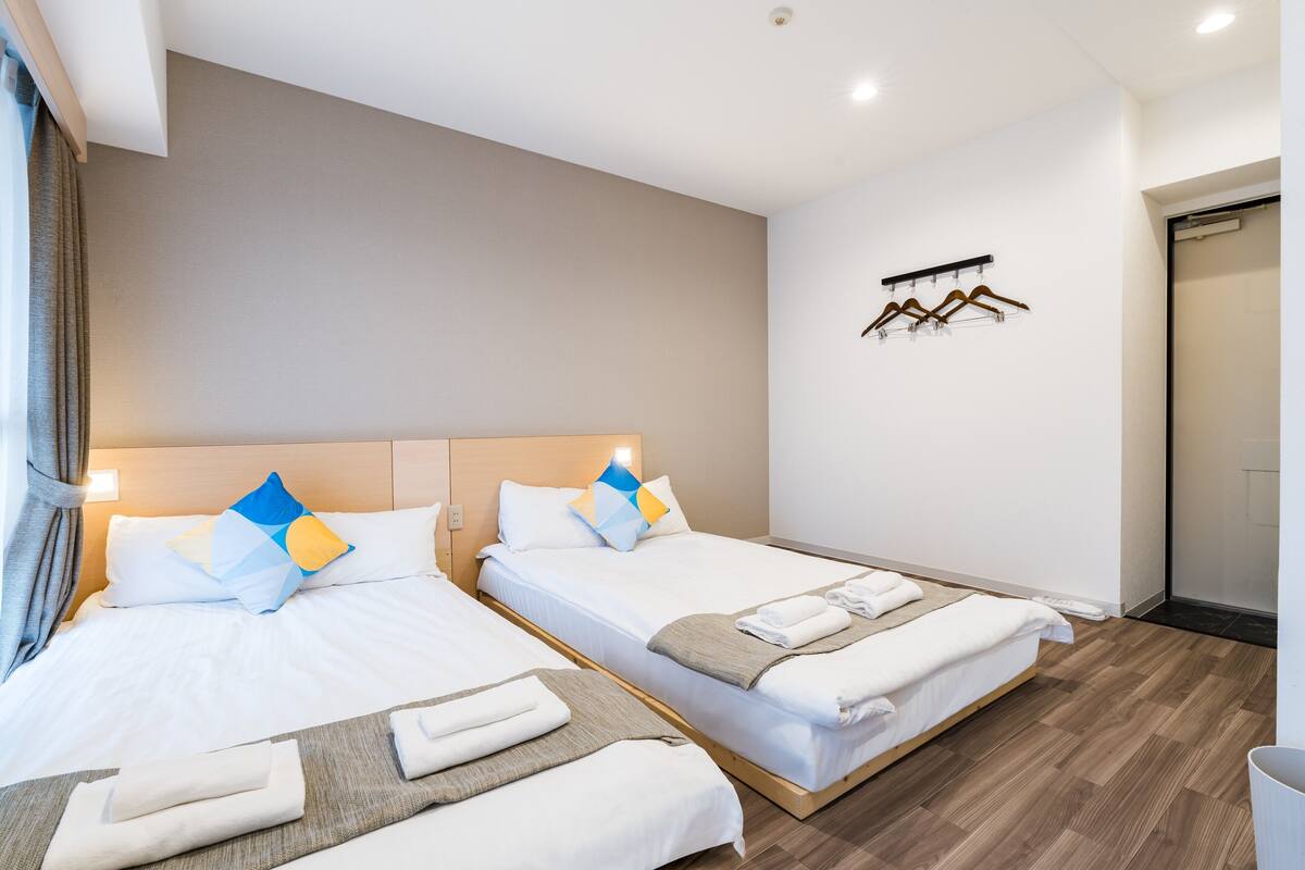 A hotel room with two beds, a wooden floor, a wall-mounted coat rack, and a door to the bathroom.