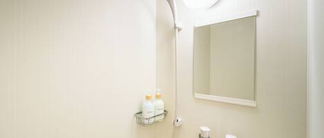 Un baño con ducha, espejo y repisa con artículos de aseo.
