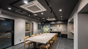 Un salón de conferencias moderno con una larga mesa, sillas, iluminación empotrada y una zona de cocina visible.