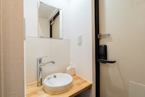 Un baño con un lavabo blanco, un espejo, un dispensador de jabón y una puerta con manija.