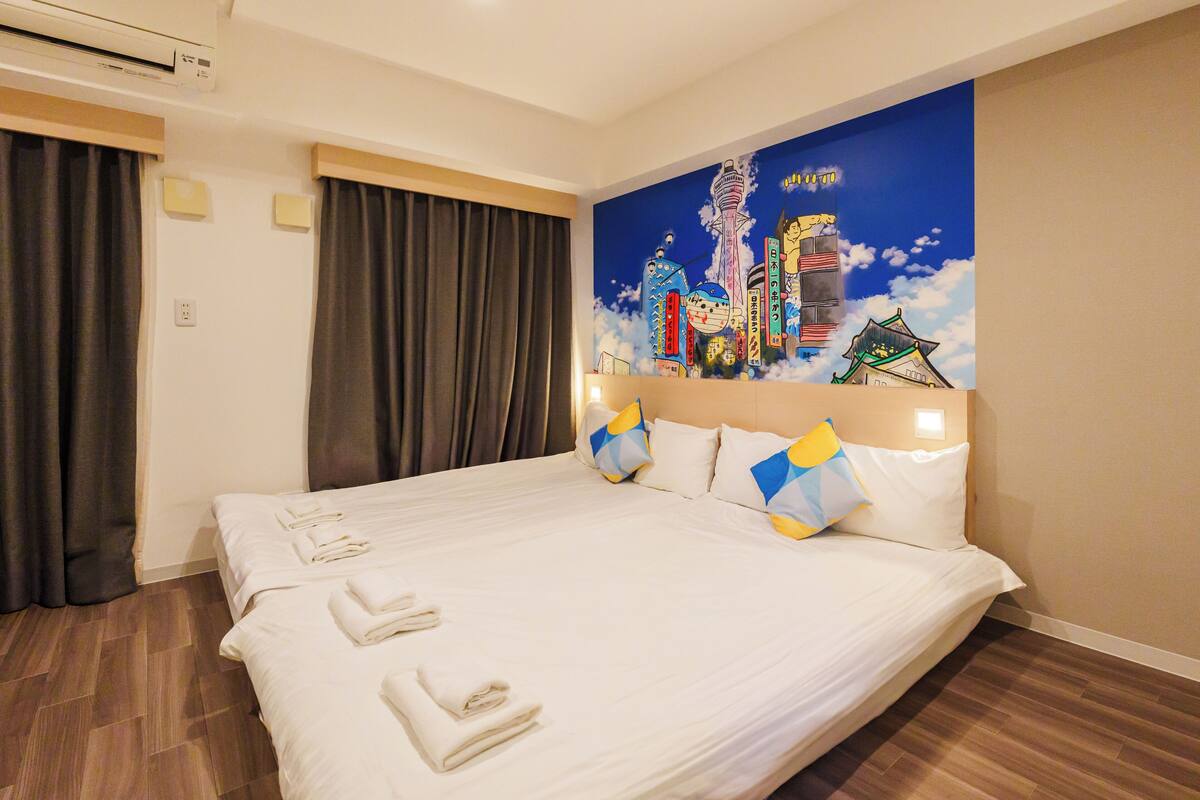 A hotel room with a large bed, a wall mural, and a window with curtains.