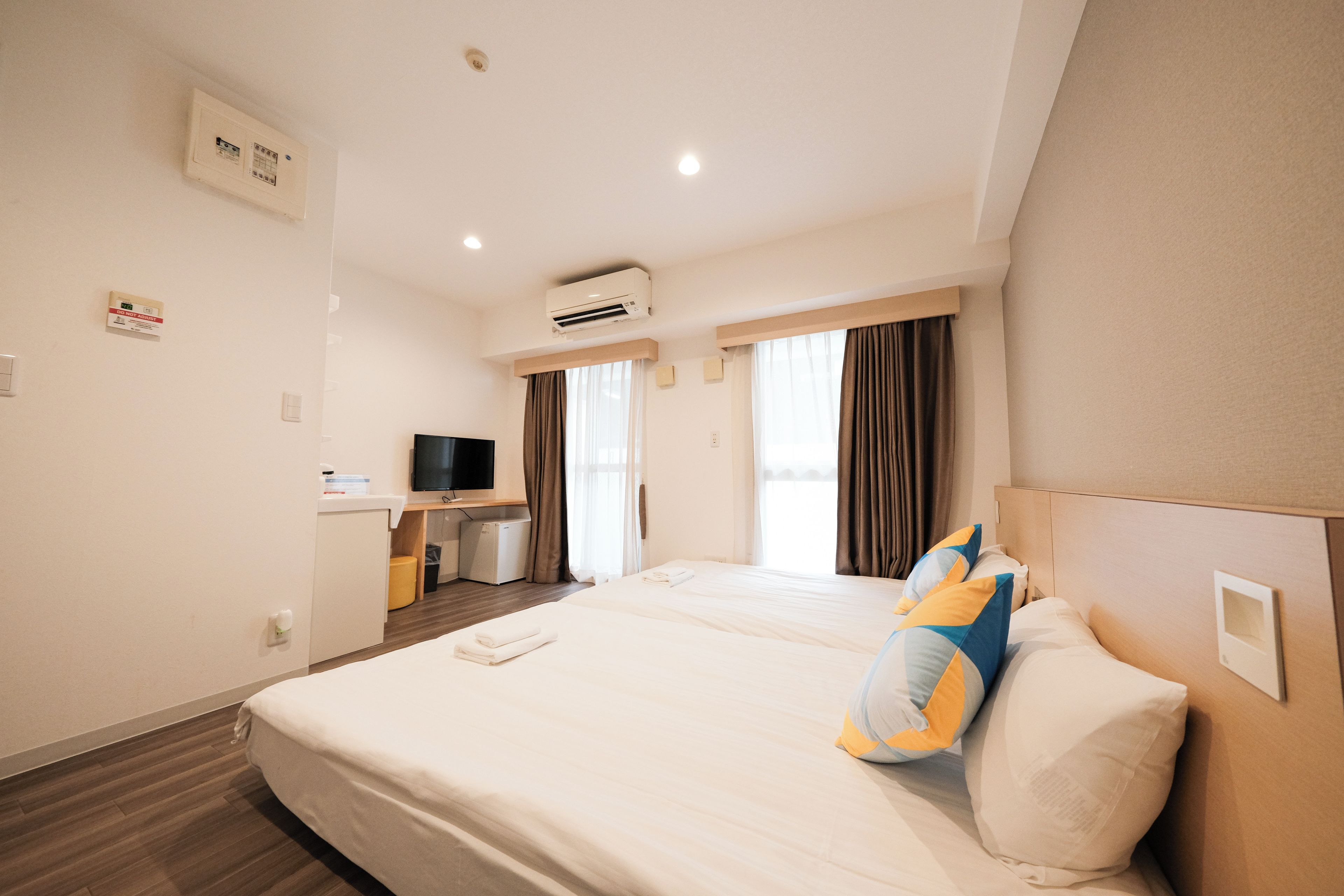 A hotel room with a bed, a television, a desk, and an air conditioning unit.