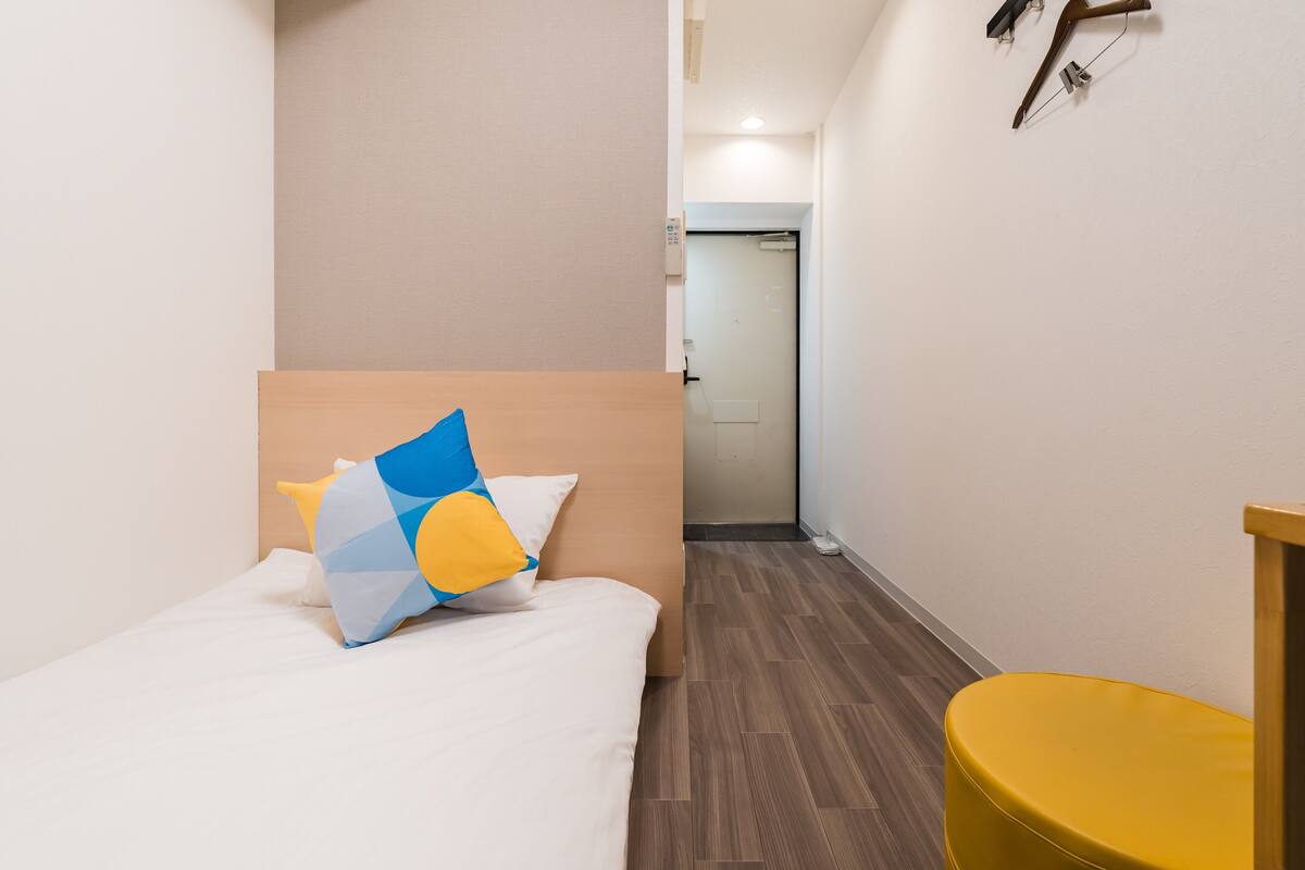 A hotel room with a bed, a yellow chair, and a wooden headboard.
