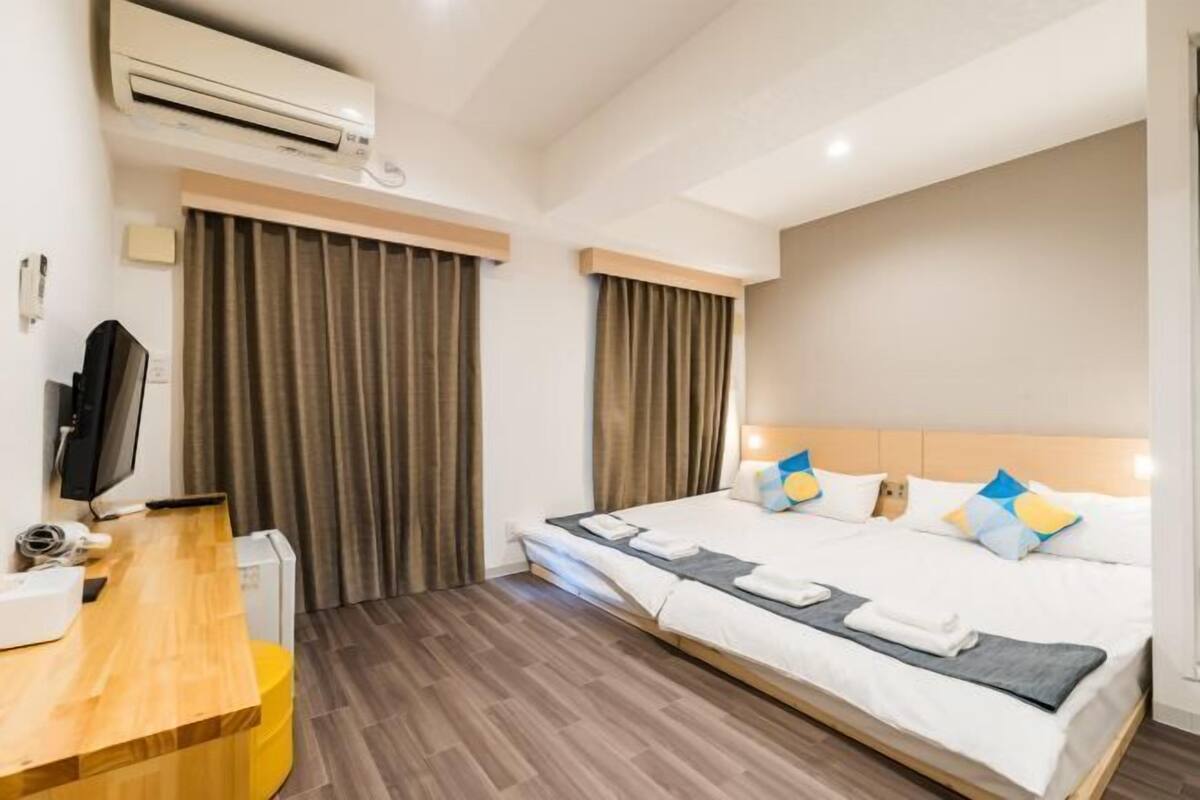 A hotel room with a bed, a desk, an air conditioner, and curtains.