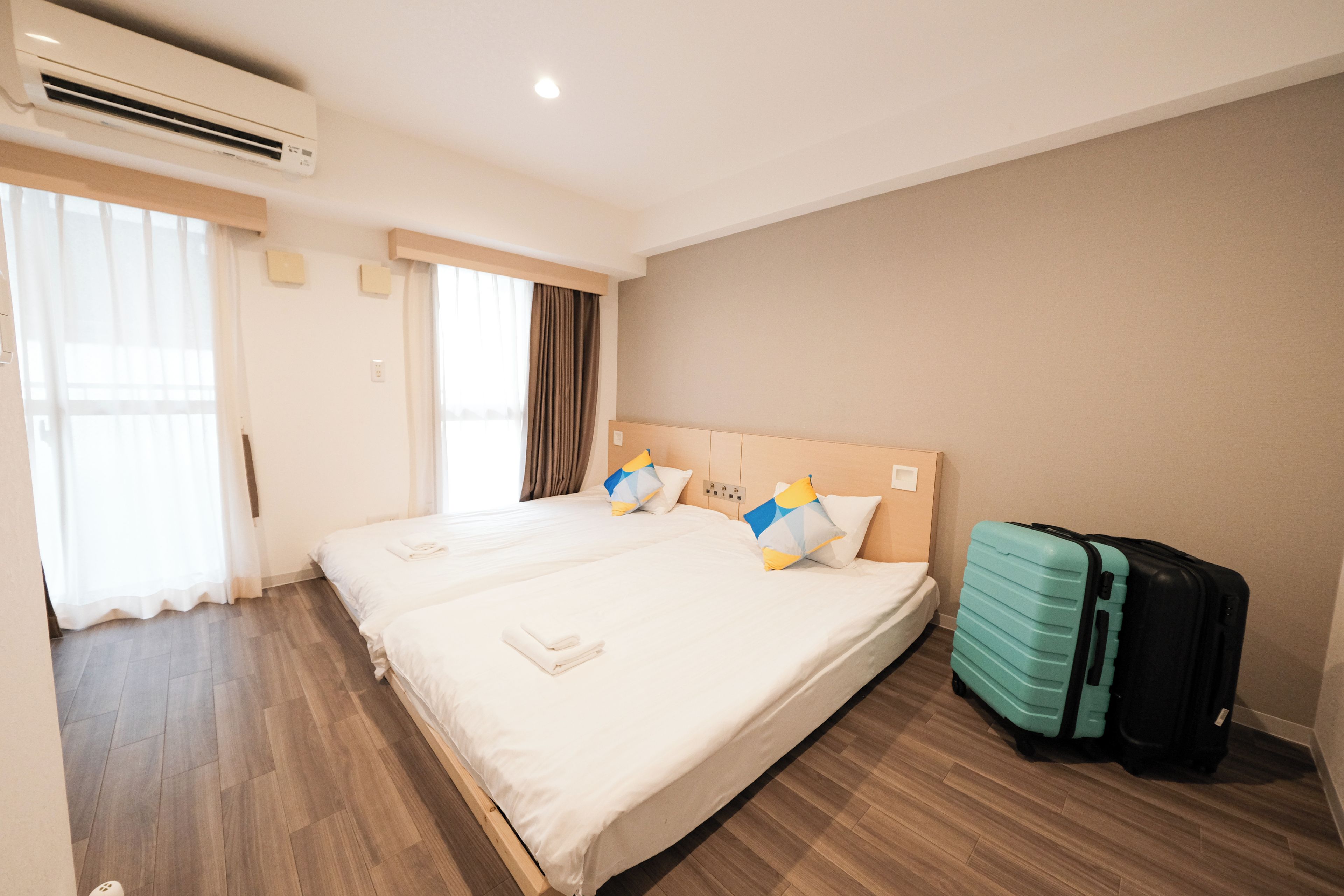 A hotel room with a large bed, a suitcase, and an air conditioning unit.