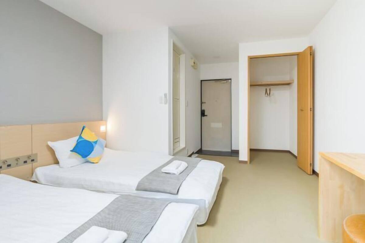 A hotel room with two beds, a wooden wardrobe, and a small wooden table.