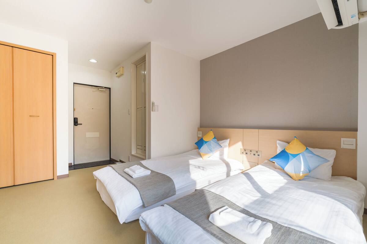 A hotel room with two beds, a wooden wardrobe, and a door leading to another room.