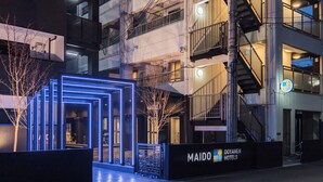 Entrada de un hotel con diseño moderno, una escalera visible y un cartel de Maido Hotels.