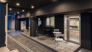 Un interior moderno con una paleta de colores oscuros, que presenta una zona de estar con sillas y una mesa, un ventanal grande y una puerta con panel esmerilado.